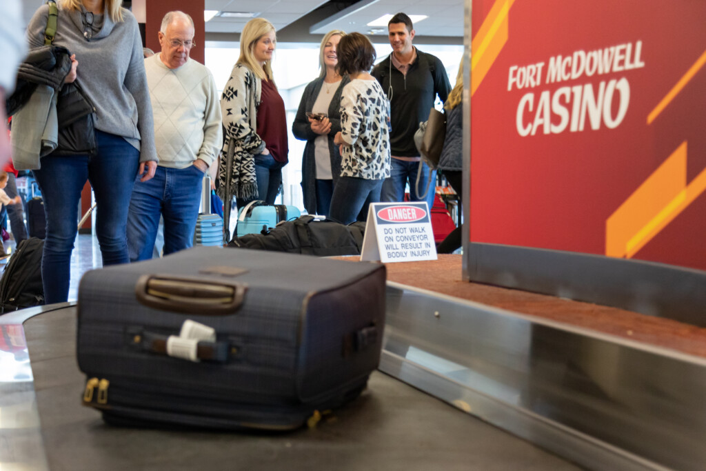 Bags on the baggage claim carousel with travelers waiting