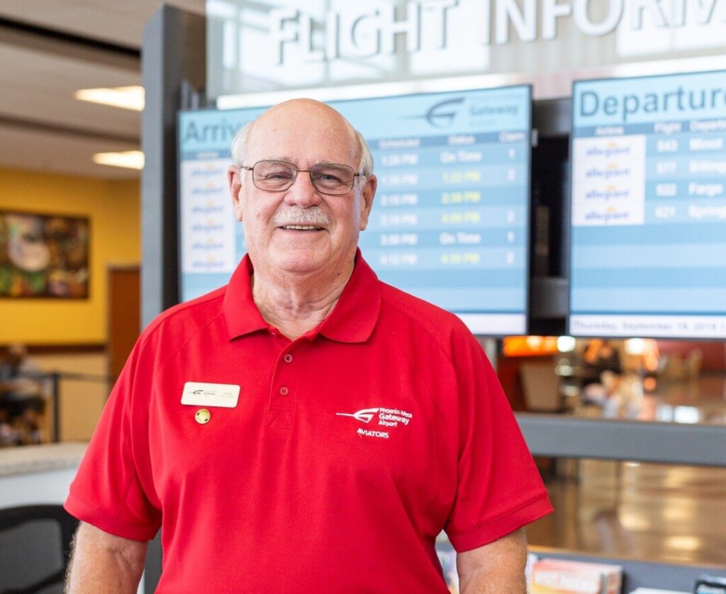 Aviator volunteer in a red shirt beside the flight information screens