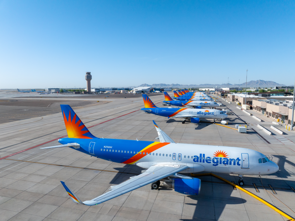 Row of Allegiant aircraft parked at the gates, with the control tower in the background