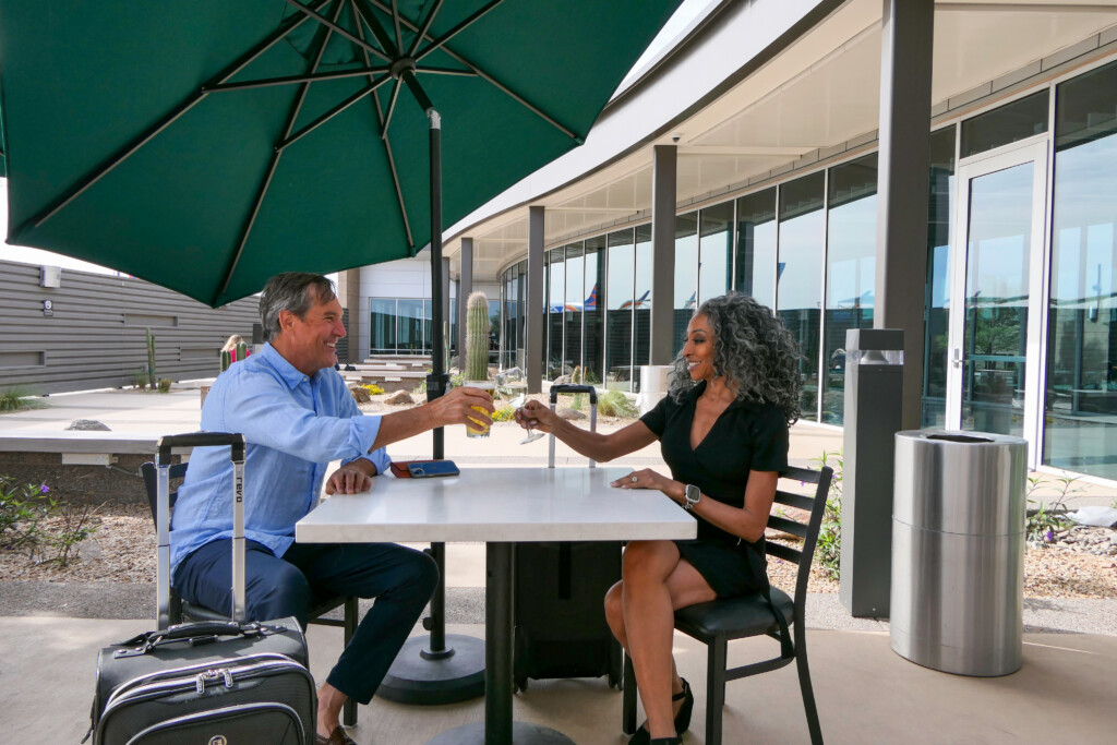Two travelers sharing a meal at an outdoor courtyard table under an umbrella