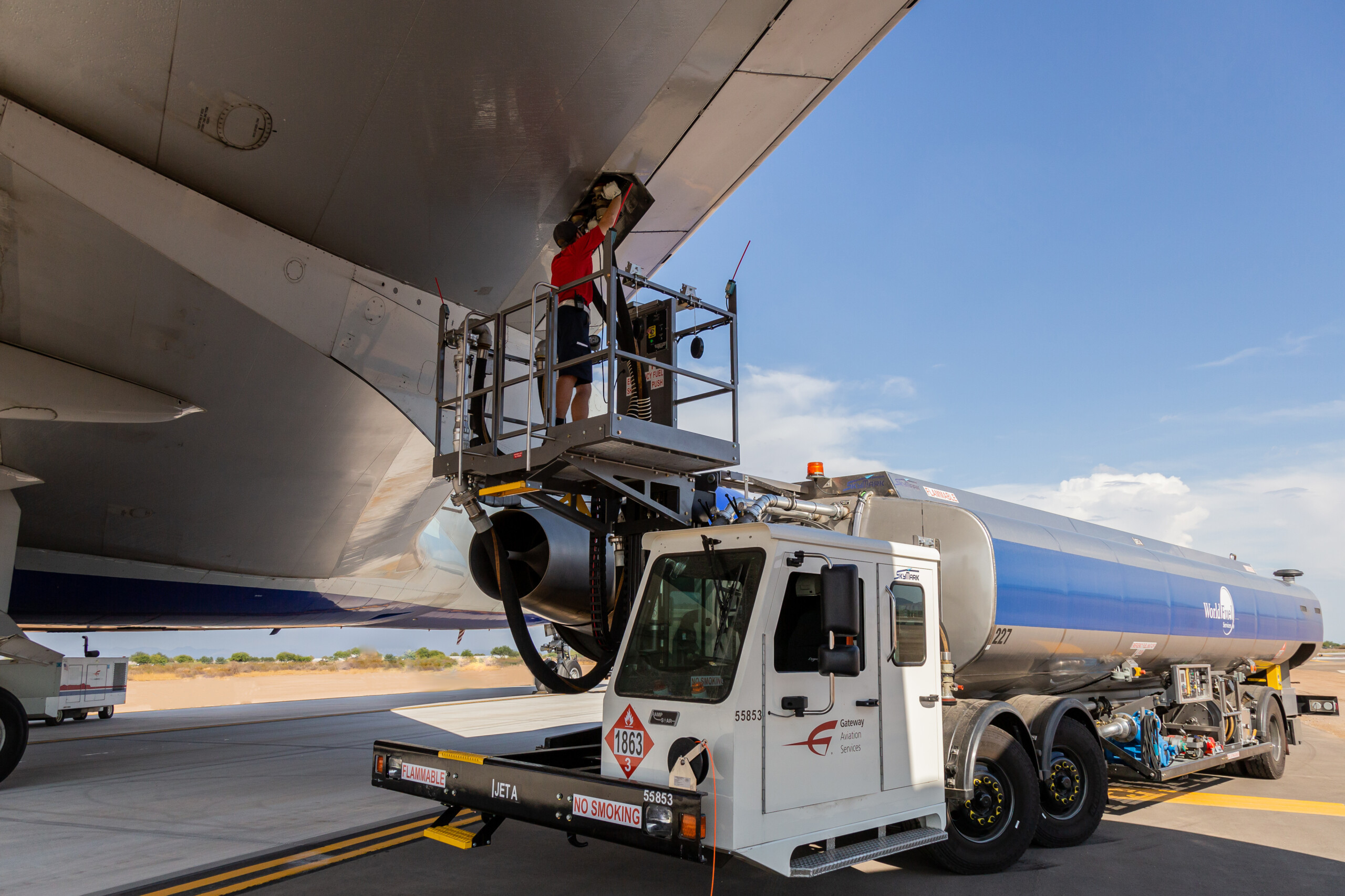 Technician on a lift servicing a large aircraft beside a fuel truck