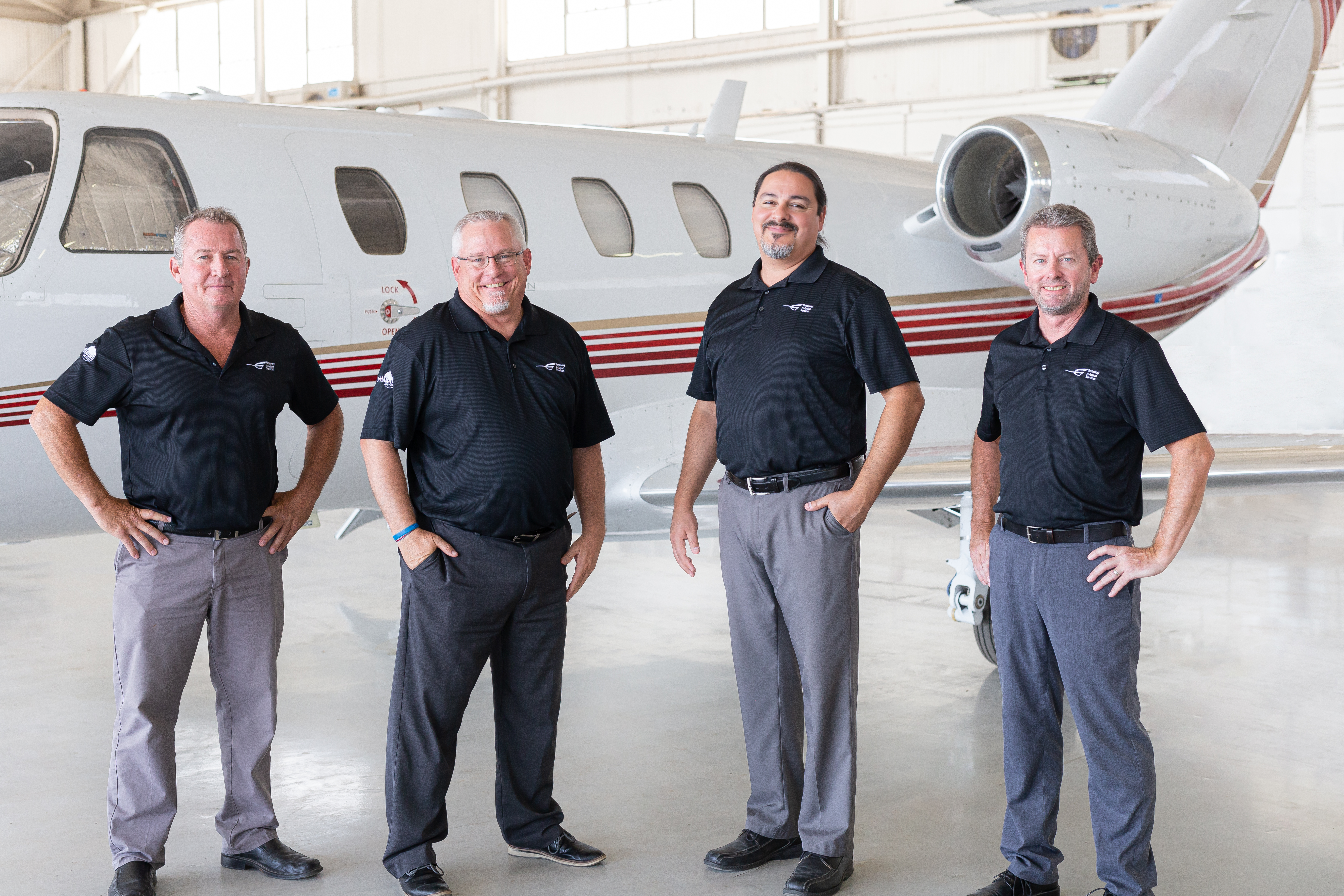 Four team members standing before a business jet in a hangar