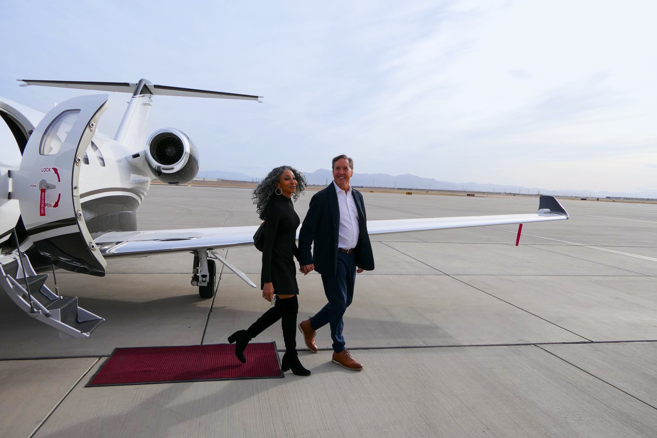 Two passengers walking from a private jet along a red carpet