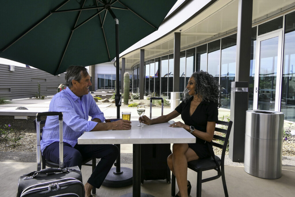 Two travelers seated with luggage at an outdoor courtyard table
