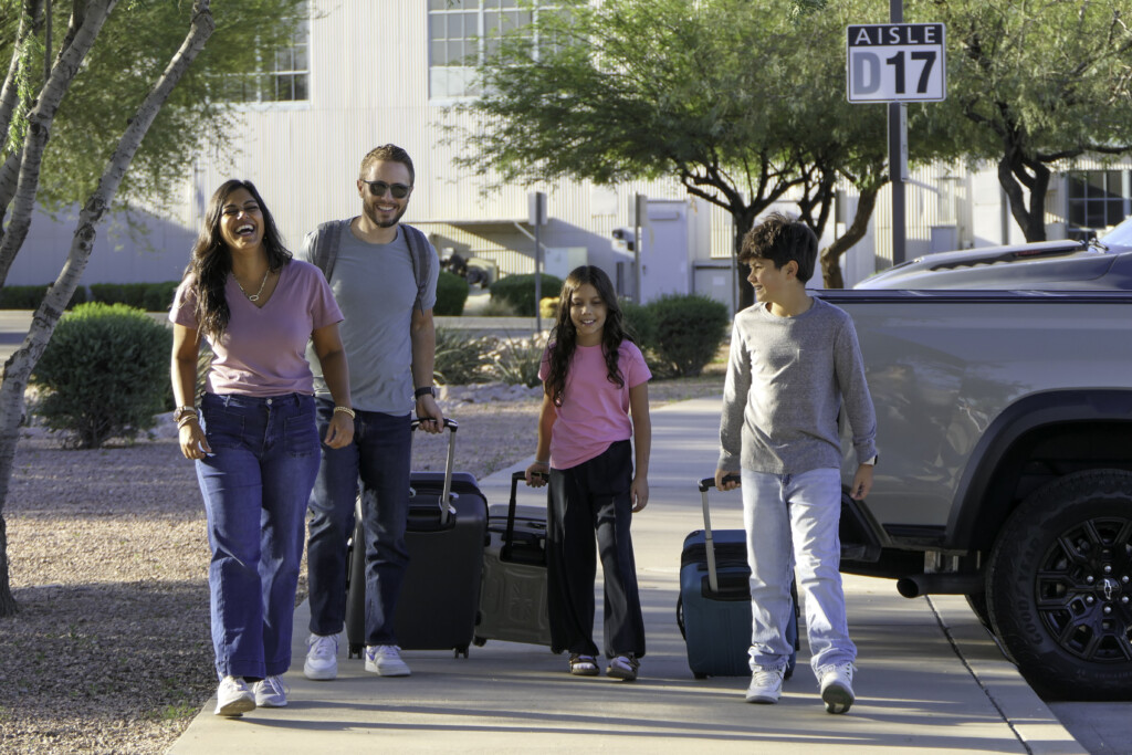 Family of four pulling luggage through the parking lot
