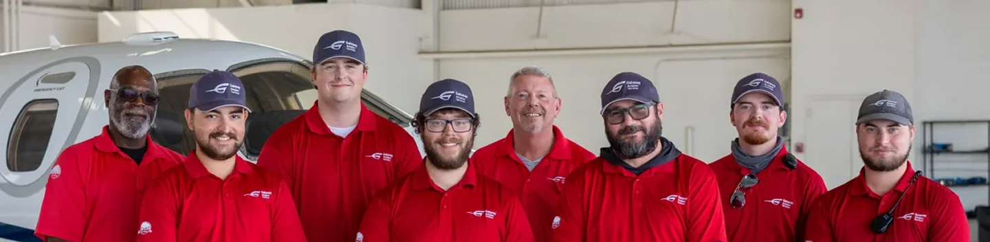 Airport team members in red polo shirts posing together in a hangar
